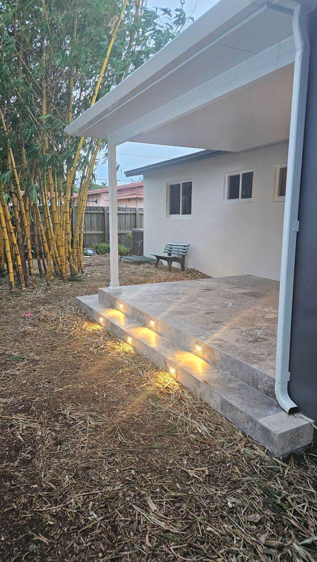 Modern concrete steps illuminated with lights lead to a small porch beside a home, framed by bamboo and a grassy area.