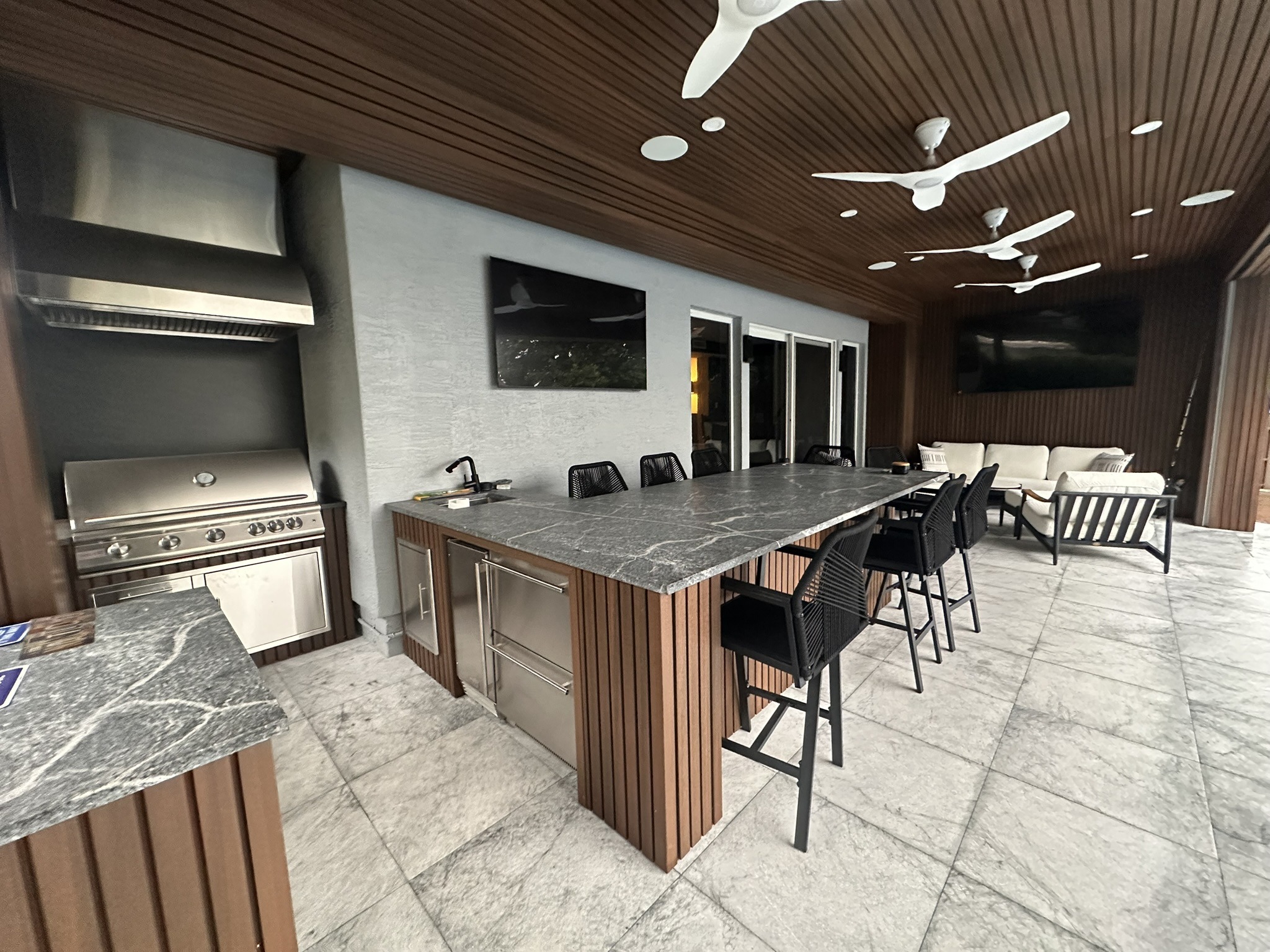 Stylish outdoor kitchen featuring a stainless steel grill, marble countertops, and seating area, ideal for entertaining and dining.
