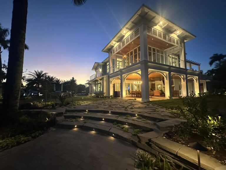 Modern two-story house illuminated at dusk, featuring large windows and a stone pathway lined with greenery. Ideal for showcasing architectural design.