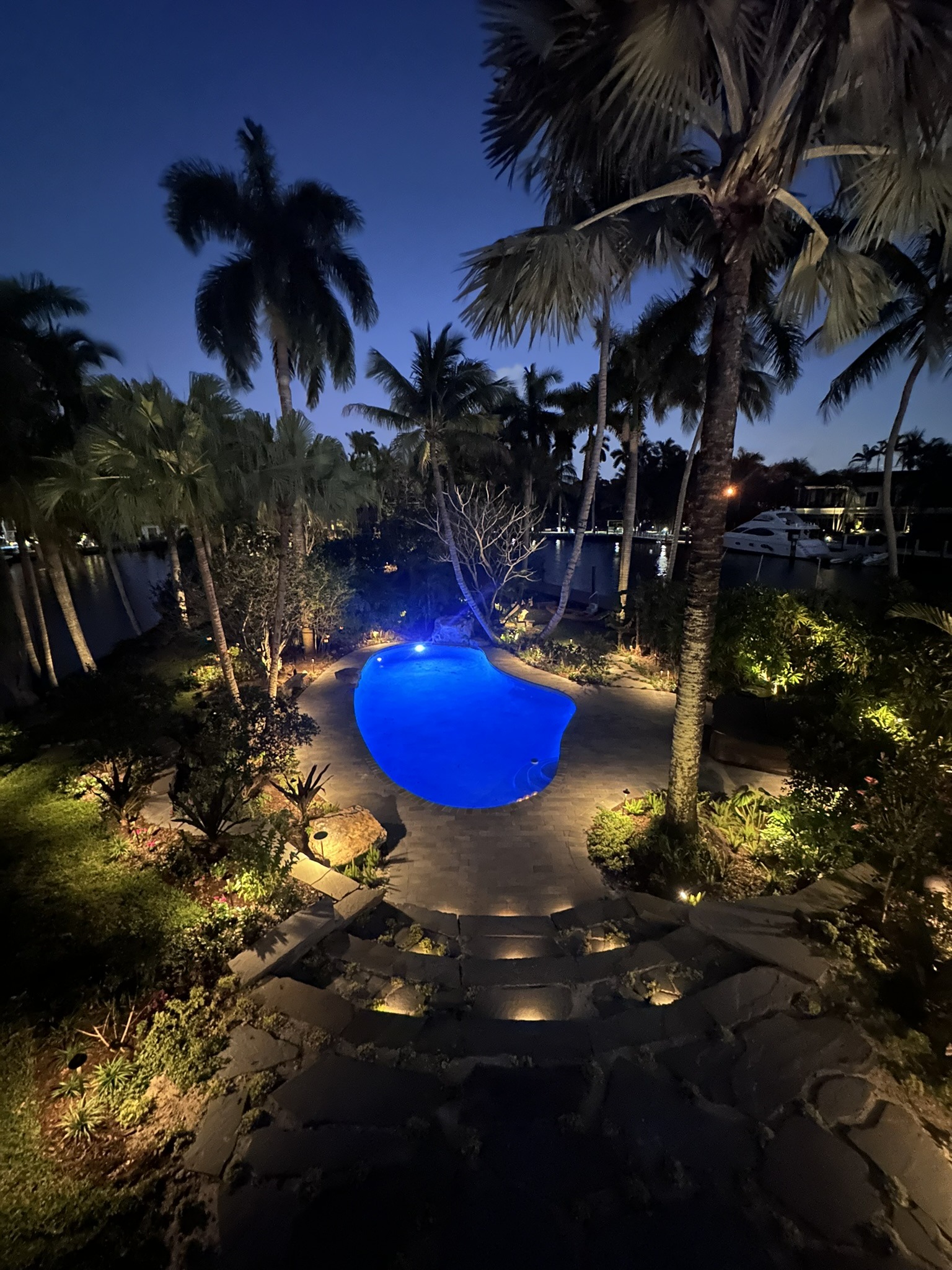 Illuminated pool surrounded by palm trees and landscaped gardens at night, creating a serene atmosphere perfect for relaxation.
